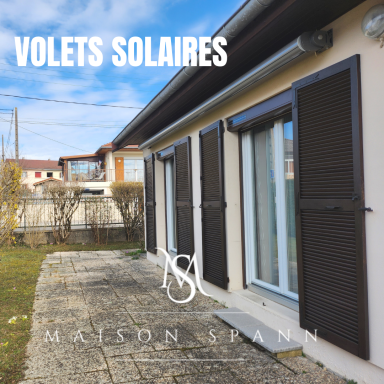 Volets solaires sur une façade de maison avec jardin et allée en pierre.
