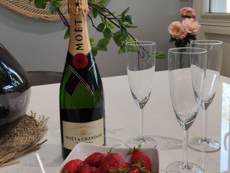 Champagne, coupes à champagne, fraises fraîches sur une table avec des fleurs en arrière-plan.