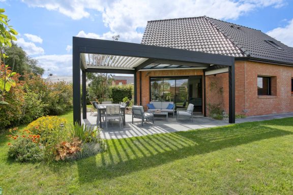 Maison moderne avec véranda, mobilier de jardin et jardin verdoyant avec pergola bioclimatique de la marque Maison Spann