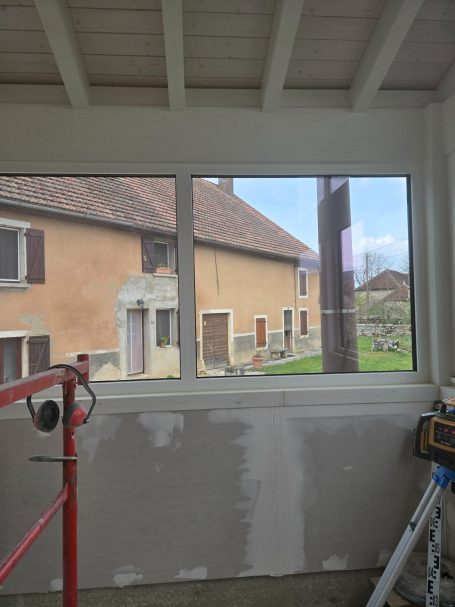 Vue à travers une fenêtre montrant une maison et un espace extérieur.