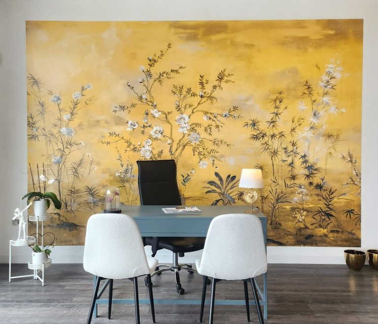 Mur jaune avec motifs floraux, bureau moderne et chaises blanches devant.