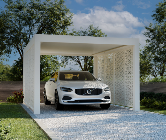 Voiture blanche garée sous un abri moderne, entourée d'un jardin verdoyant.