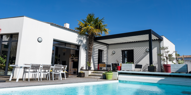 Villa moderne avec piscine, terrasse et palmier sous un ciel bleu avec pergola bioclimatique de la marque Maison Spann