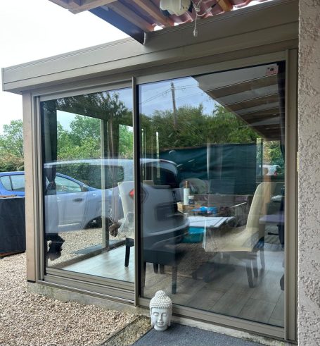 Véranda moderne avec glaces et meubles, vue sur un jardin.