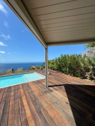 Vue sur une piscine et l'océan depuis une terrasse en bois avec pergola bioclimatique de la marque Maison Spann