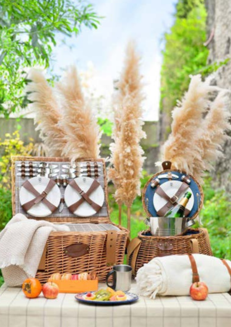 Panier de pique-nique avec des pampas et une décoration de jardin. Fruits et serviettes à côté.