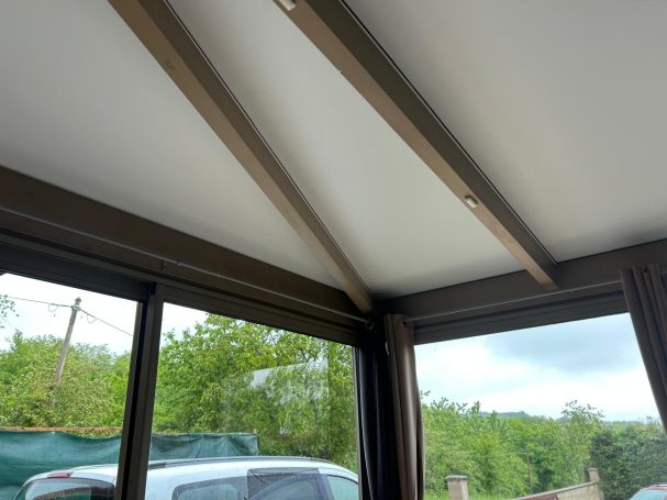 Vue intérieure d'un bâtiment avec des poutres au plafond et des fenêtres sur l'extérieur.