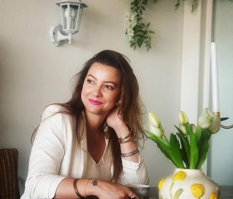 Femme souriante avec des cheveux bruns, assise à une table avec une tasse.