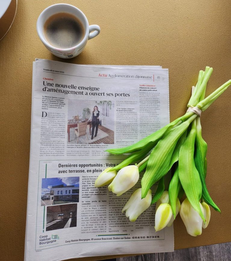 Un journal ouvert, une tasse de café et un bouquet de tulipes blanches sur une table.