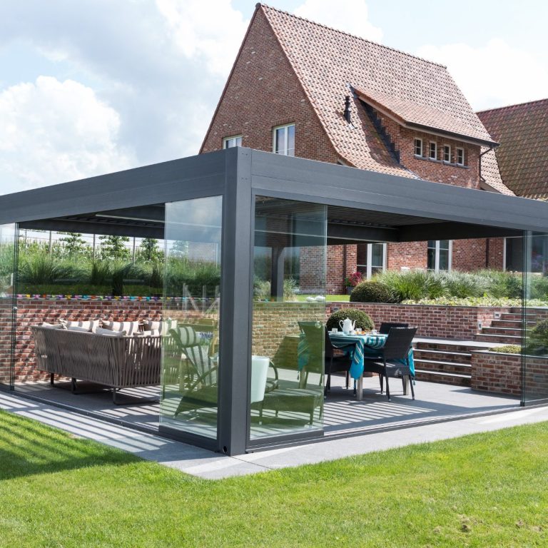 Terrasse moderne avec pergola à paroi en verre, mobilier extérieur et maison en arrière-plan.