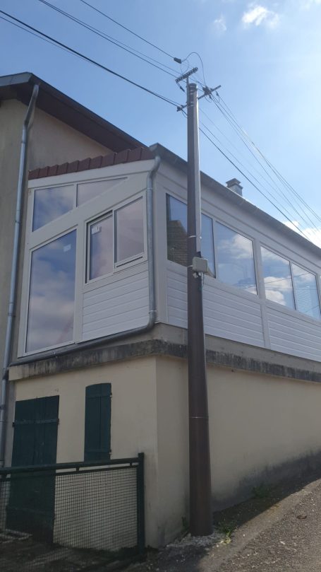 Véranda en bois blanc sur un mur, avec un poteau électrique à proximité.