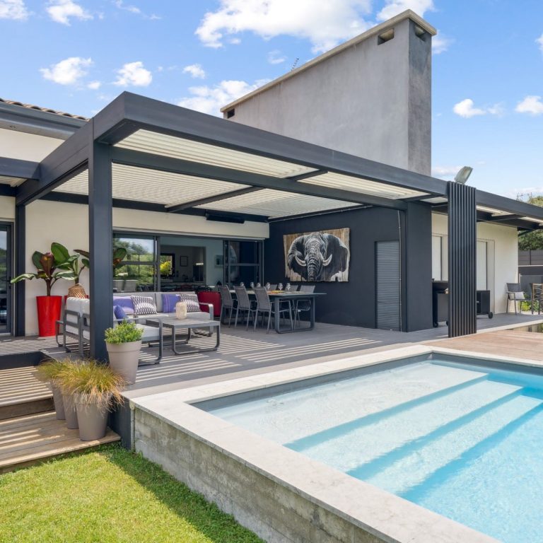 Maison moderne avec piscine, terrasse avec pergola bioclimatique et espace repas en extérieur. Ciel dégagé.