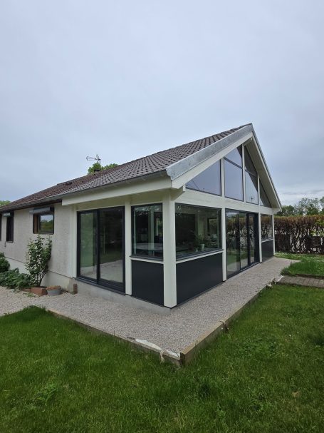 Maison moderne avec de grandes fenêtres et une véranda sur un jardin.