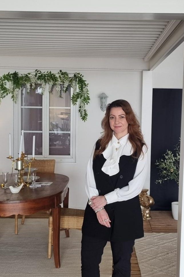 Femme debout dans un magasin d'exposition, sous une pergola blanche Solisystème, avec une table en bois et des plantes décoratives.