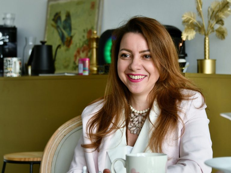 Femme souriante avec des cheveux bruns, assise à une table avec une tasse.