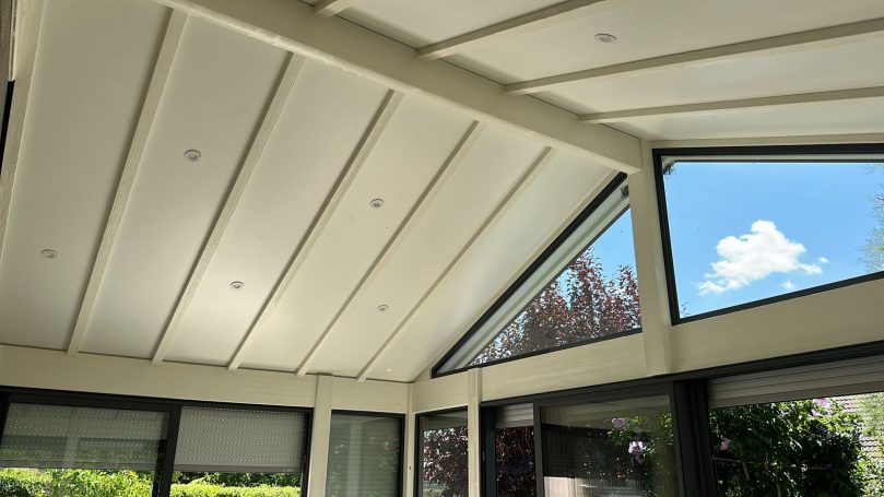 Plafond moderne en bois, fenêtres angulaires avec vue sur le ciel et la végétation.