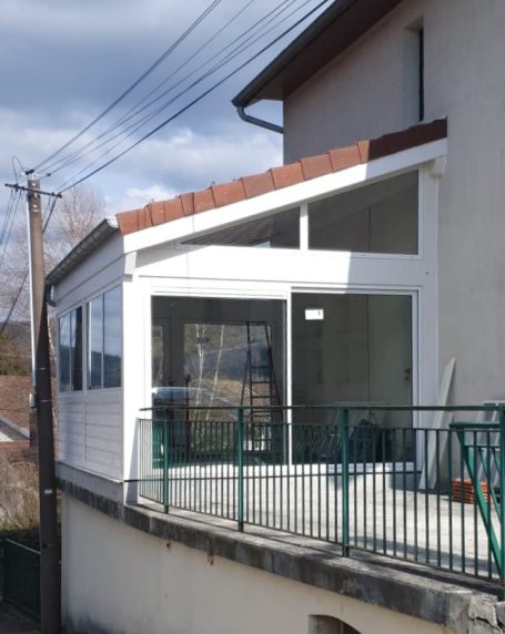 Véranda moderne en bois blanc, avec balustrade verte, à côté d'une maison.